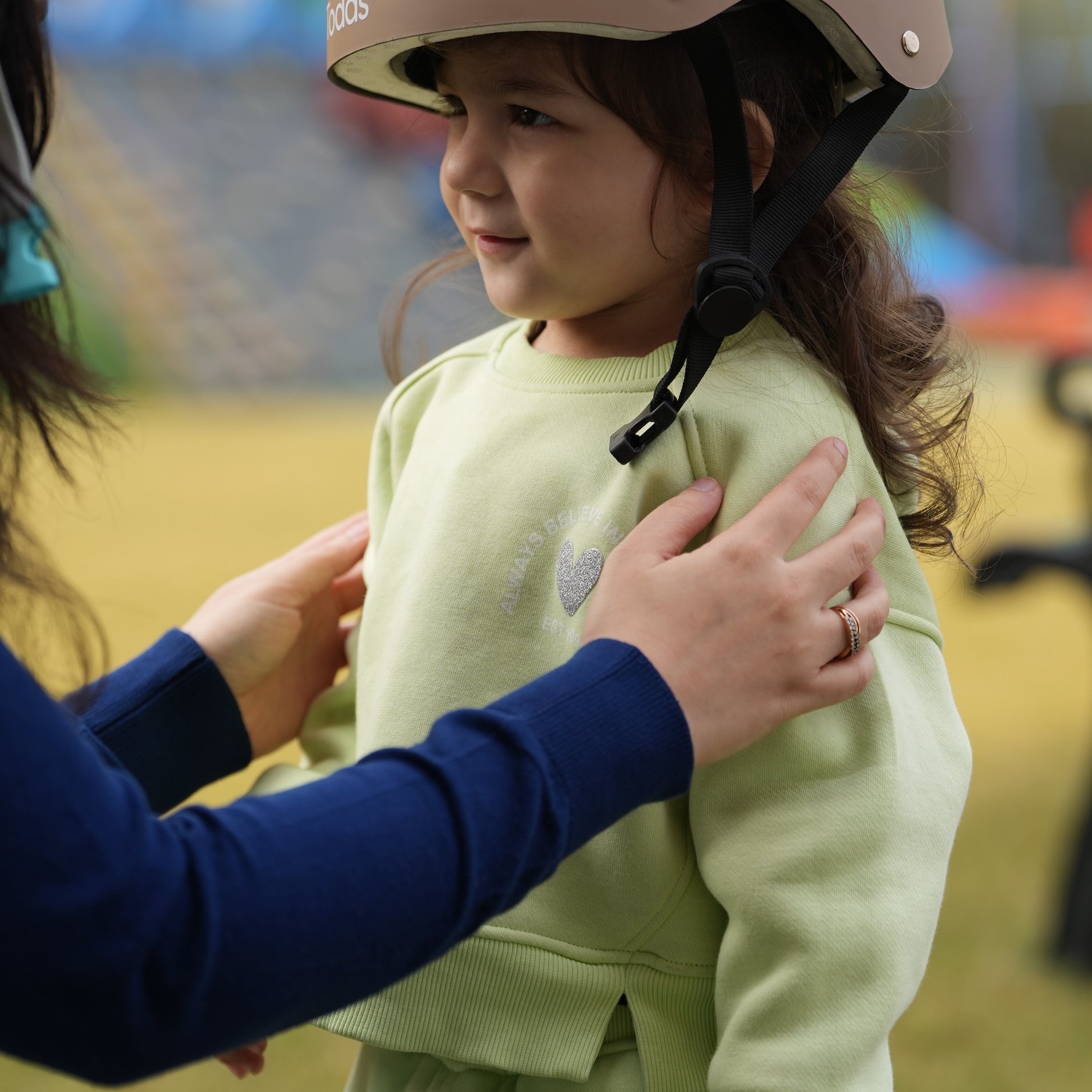 Child wearing a helmet with an adult adjusting it, outdoors.