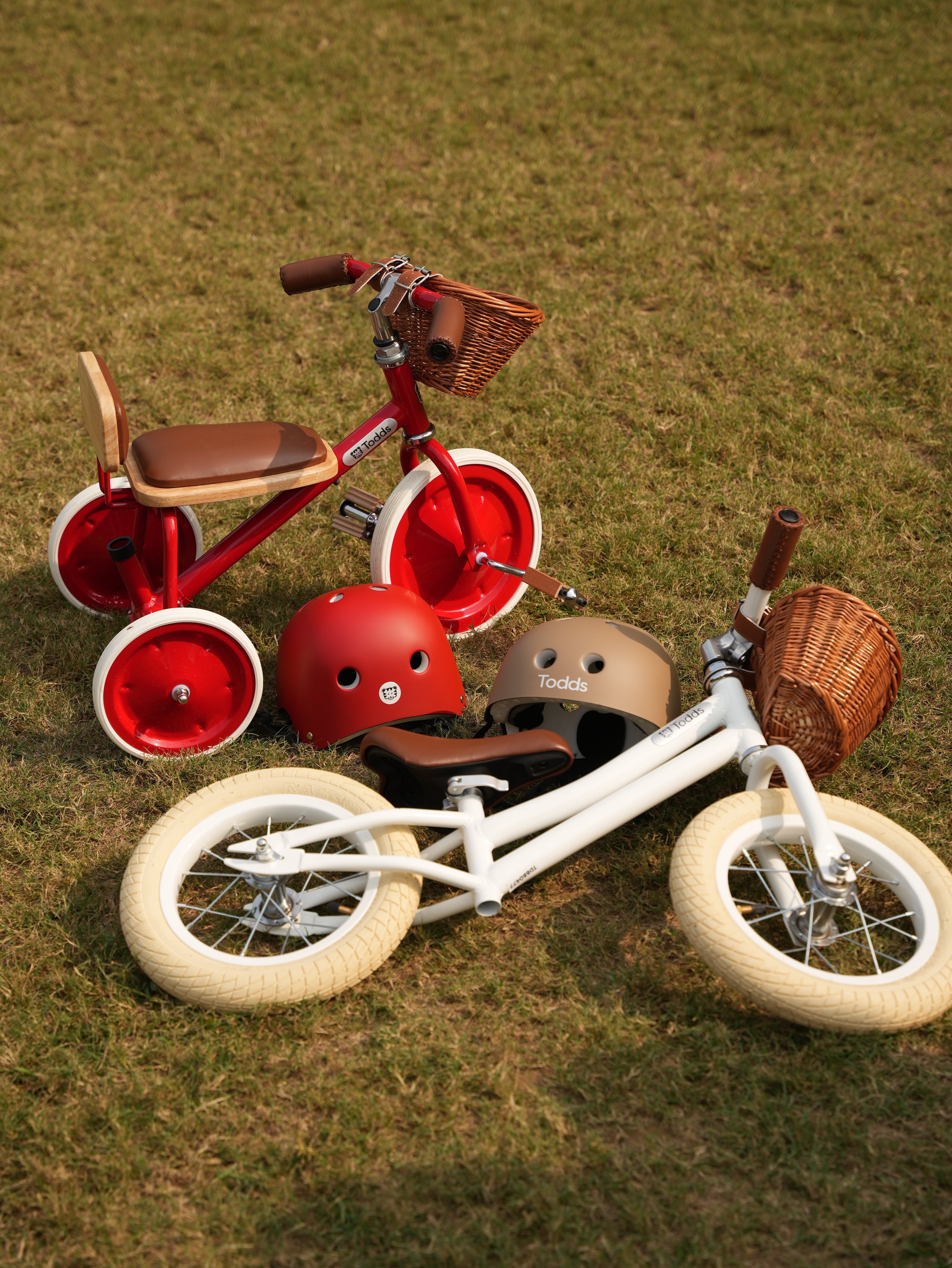 Two children's tricycles and helmets on a grassy field